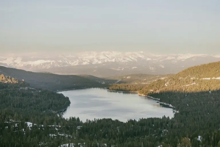 a lake surrounded by trees and snow covered mountains